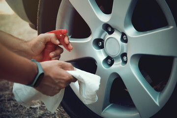 Man with towel and spray bottle about to wash car wheels
