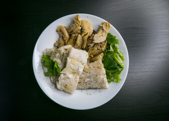 Hake fish with artichokes, parsley, fine herbs and green salad with olive oil. Top view