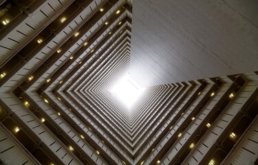 Low angle diminishing perspective view from the atrium of a multistorey public housing in Hong Kong, with sunlight cast from the top and the multilayers of corridors making a unique geometric pattern - obrazy, fototapety, plakaty