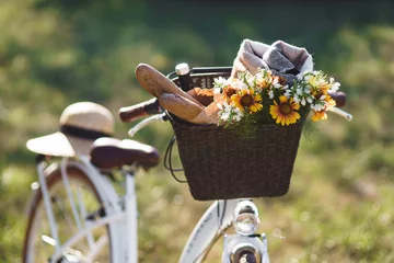 Poster Wicker basket with bread baguette, flowers and a picnic blanket in a park on a sunny day © Ksenia