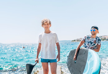 Portrait of blonde teenage boy and his smiling father surfers carrying the surfing board on the...