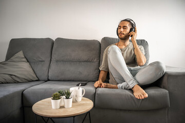 Hombre con moño, barba, camiseta verde suave y vaqueros azul claro escuchando música con su...