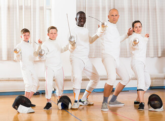 Portrait of happy adult and teenagers fencers in full fencing outfit standing in gym