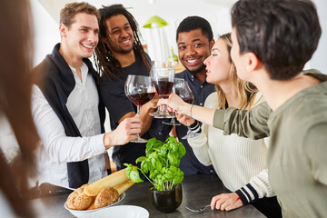 Friends toasting with glass of red wine in kitchen