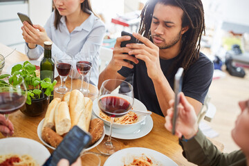 Friends look at smartphone while eating at the table - obrazy, fototapety, plakaty