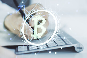 Double exposure of creative Bitcoin symbol with hand writing in notebook on background with laptop. Cryptocurrency concept