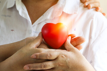 A hand of old woman holding a red heart symbol in hands, healthy care concept