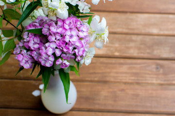 Bouquet of wildflowers in a vase on a wooden background. Violet and white flowers in a vase.