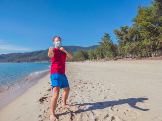 Young muscle man in medical mask perform outdoor workouts in the park near sea during second wave...