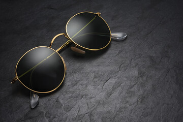 Gold frame round black sunglasses on black slate background.