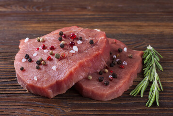 raw beef steak with rosemary on brown wooden background