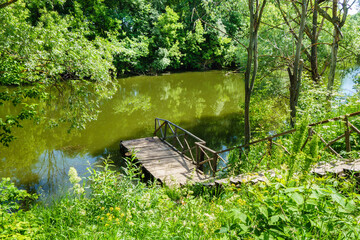 Wooden staircase descending to quiet river or lake. Surrounding landscape filled with flowering...