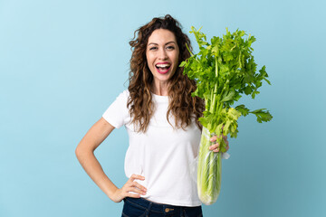 Young woman holding a celery isolated on blue background with surprise and shocked facial expression