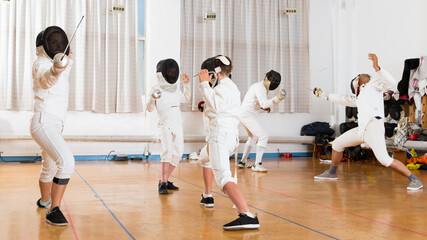 Adults and teens wearing fencing uniform practicing with foil at gym