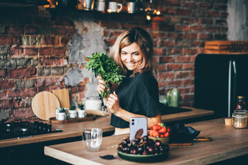 Professional cook fixes smartphone to film and takes greenery of fresh spices from brown wooden board on special table.