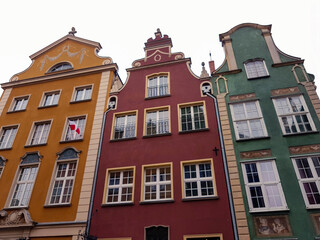 Three colorful old houses in Gdansk with a Polish flag outside a window on a grey day.
