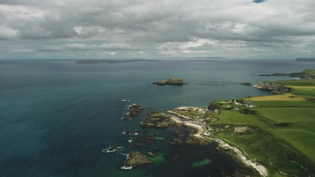 Cliff aerial landscape: rocky ocean shore. Irish plant distillery against backdrop of nature: meadows and cumulus clouds on summer day. Industrial scenery of bird's-eye view. Shooting shot in 4K UHD