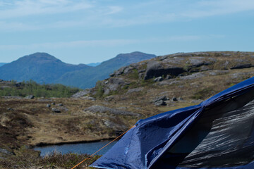 Blue tent with mountains and a lake in the background, blue skies