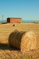 Straw bales during collection in the summer and with a warehouse in the background