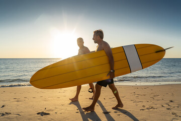 Two senior surfers with surfboard having fun on empty remote beach enjoying retirement lifestyle