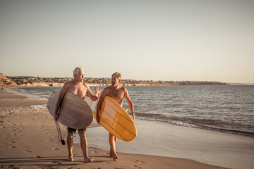 Two senior surfers with surfboard having fun on empty remote beach enjoying retirement lifestyle