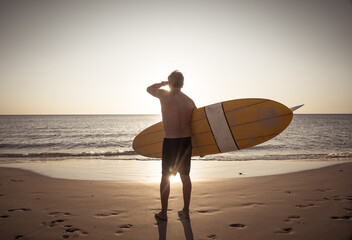Fototapeta na wymiar Portrait of mature senior Surfer looking at the ocean with vintage surfboard on an empty beach