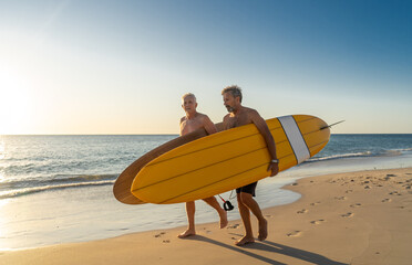 Two senior surfers with surfboard having fun on empty remote beach enjoying retirement lifestyle
