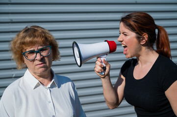 A middle-aged woman yells at an elderly mother through a megaphone. Quarrel between generations.