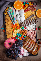 Christmas sweets platter. Christmas fruit cake, candy, chocolate, candy cane, cookies, fruit on black tray, top view. Christmas food concept.