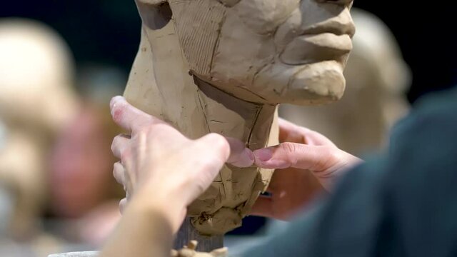 Woman sculptor at work on a sculpture of a human head. The process of restoring the shape of the neck. Side view. Close up view.
