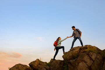 Travelers Hiking in the Mountains at Sunset. Man Helping Woman to Climb to the Top. Family Travel and Adventure.