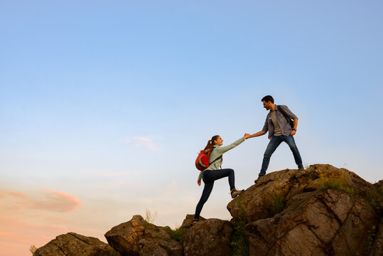 Travelers Hiking in the Mountains at Sunset. Man Helping Woman to Climb to the Top. Family Travel and Adventure.