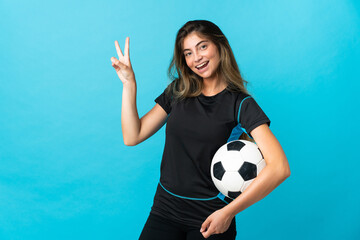 Young football player woman isolated on blue background smiling and showing victory sign