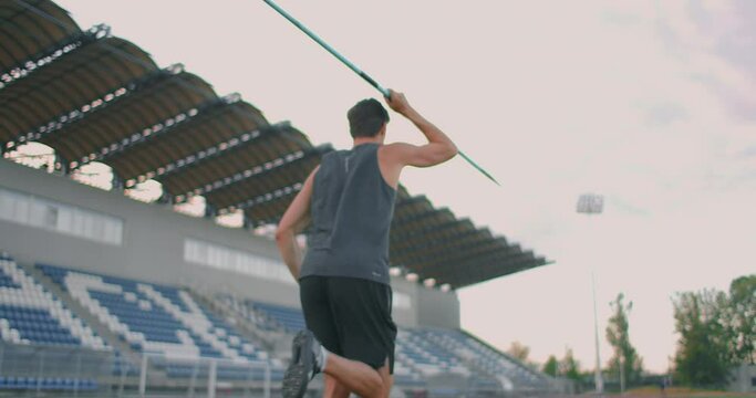 Sportsman doing javelin throw on athletic ground. Male athlete throwing the javelin in the olympic stadium. Athlete in sport clothes at athletic sport track in professional stadium