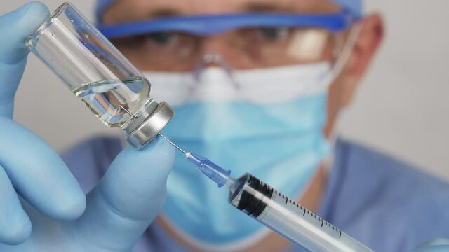The male doctor prepares an injection to a patient. Needle injected in the ampule with a liquid drug. The doctor draws medicine into a syringe from an ampule
