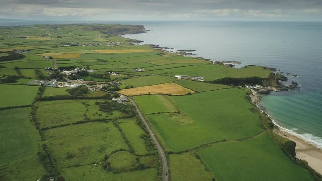 Ireland aerial green fields landscape shot: road along meadows. Wide plants and farms on rocky coastline of Atlantic ocean. Epic scenery of Northern Irish Island. Panoramic shooting in 4k, UHD