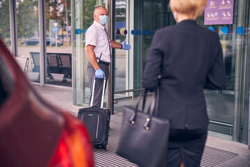 Airport male worker helping elegant lady to carry luggage