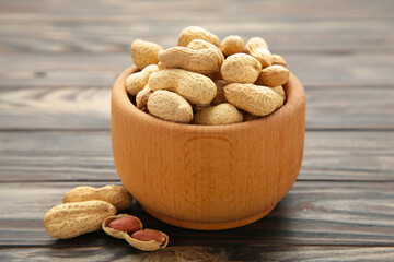 Dried peanuts in wooden bowl on brown wooden background.