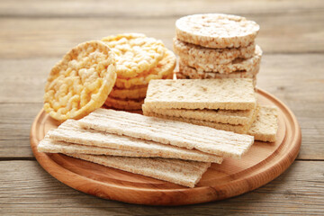 Various types of healthy whole grain crispbreads on cutting board on grey wooden background.