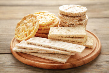 Various types of healthy whole grain crispbreads on cutting board on grey wooden background.