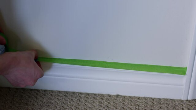 Man taping baseboards with painters tape - close up on hands