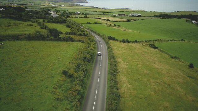 Ireland car riding road aerial view: rural green pasture and meadows in Irish. Coastline on horizon with ocean bay. Picturesque landscape of farmland in summer day. Footage shot in FullHD