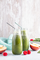 Two glass bottles of green smoothie with spinach, raspberry and apple on concrete table, still life. Healthy freshly blended smoothie for summer heat wave, vertical image