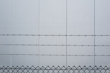 Barbed wire over mesh fence against concrete wall with copy space