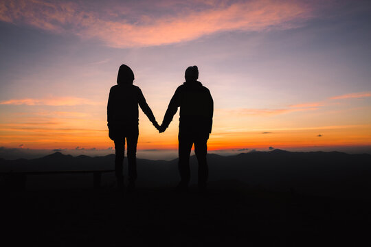 silhouette of a man and woman holding hands with each other  with a beautiful sunset in background.  happy lifestyle concept.