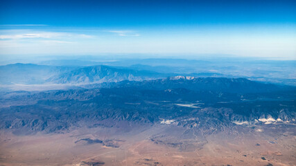 Beautiful mountains and valleys of the desert American southwest with red, blue and green scenery viewed from the airplane with white puffy clouds