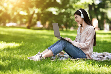 Happy Asian Girl Freelancer Working On Laptop In Park And Listening Music
