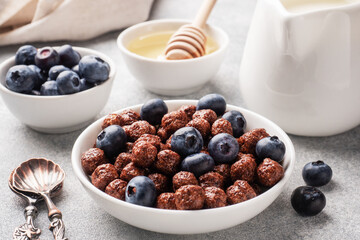 Chocolate flakes made from natural cereals with fresh blueberries, honey and milk. The concept of a healthy wholesome Breakfast. Grey concrete background