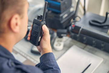 Cheerful adult male looking down while saying on the walkie talkie