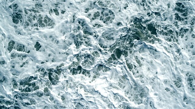 View from Top over coastal storm waves. Drone Topdown with blue waves and white foam. Empty aerial wide shot with no people.